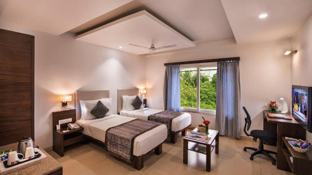 A spacious and well-lit hotel room with twin beds, chairs, a table, and decor in light pastel tones at Lords Eco Inn Jayanagar Bangalore.