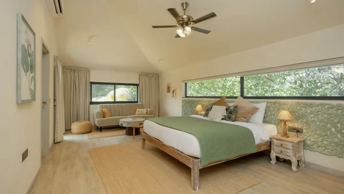 Bedroom of Lime Tree Hotels & Service Apartment Private Limited featuring a wooden beam ceiling, a ceiling fan, and large windows with natural light.