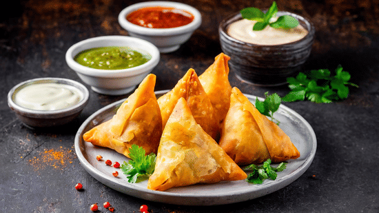 Plate of samosas served with green chutney, red sauce, and yogurt.