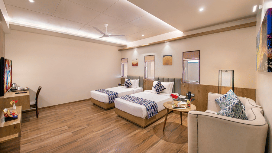 A well-furnished, wooden floored hotel room with twin beds, a work desk, and a couch in Lords Inn Jmanagar