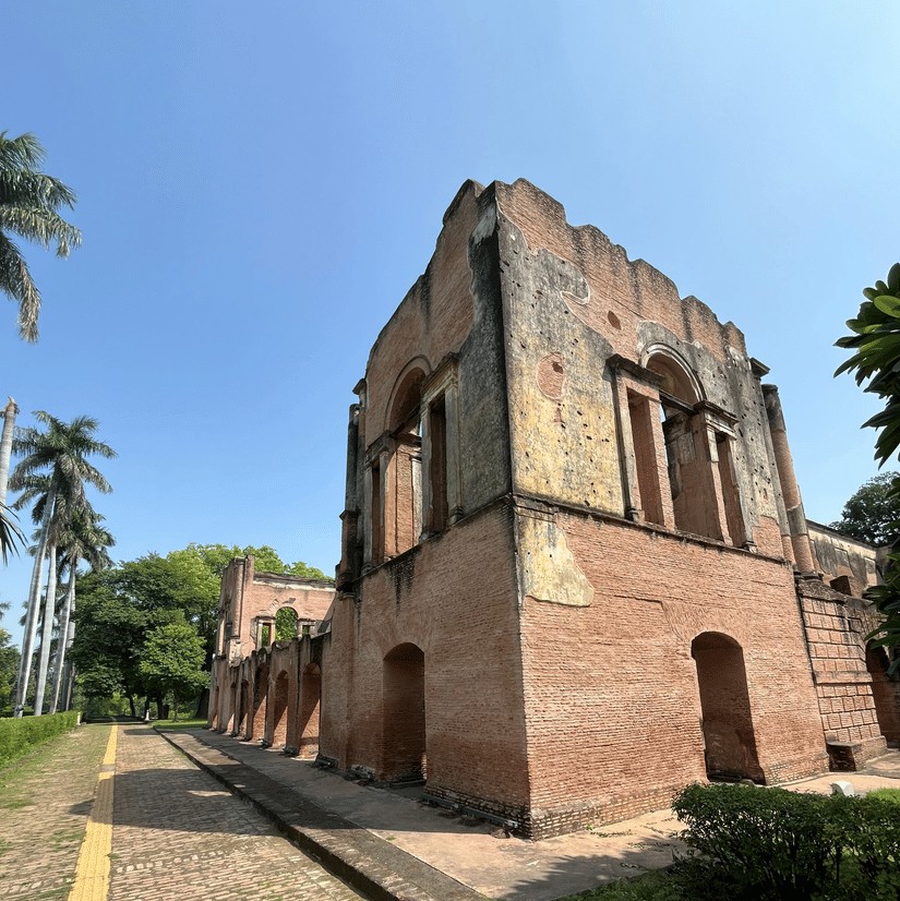 Ruins of the rooms of The Residency, Lucknow, with a broad pathway running in front with trees lining  the pathway.