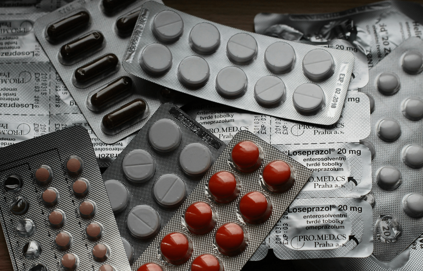 A close-up image of various packs of pills scattered on a surface. The pills are in different sizes.
