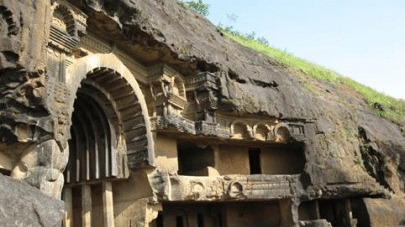 An overview of the Bhaja Caves in Khandala with a person standing in front of it and blue sky in the background. These caves are one of the most popular Khandala hill station tourist places.