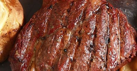 A close-up shot of a large, grilled steak with visible grill marks and a rich brown color