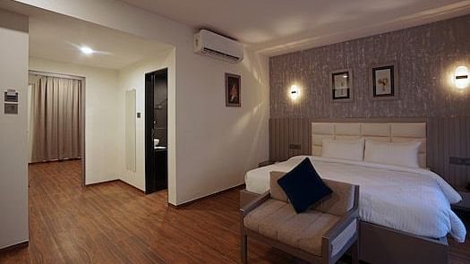 Spacious room at Grand Continent, Anjuna featuring a large bed, a sofa, dark curtains, decorative wall lights, and an open doorway.