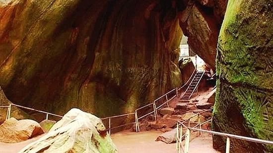 A cave entrance with rocks features a person walking inside, revealing a natural cavern. - Wayanad