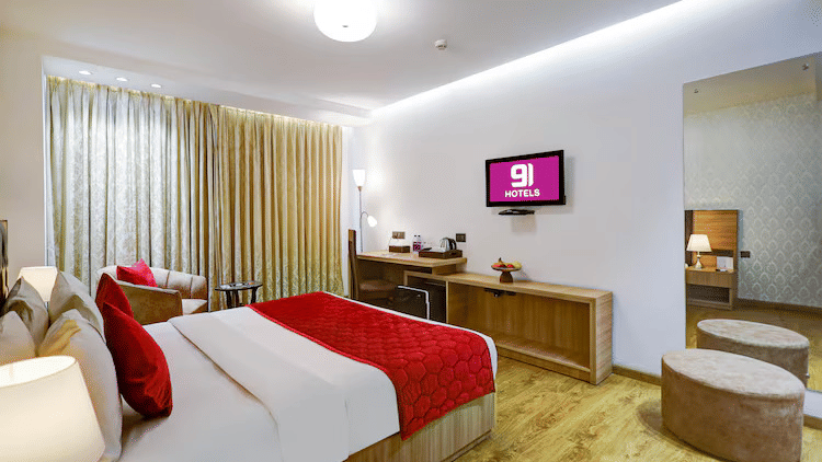 A bright and modern hotel room featuring a king size bed with a bold red runner, light wood flooring, and a wall-mounted flat-screen TV - Hotel 91 HUDA City Centre, Gurugram