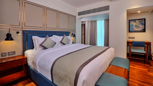 Well-lit Premium Suite at Pride Hotel Udaipur featuring a plush bed with a rectangular ottoman at its foot and a work desk in the background facing the wall