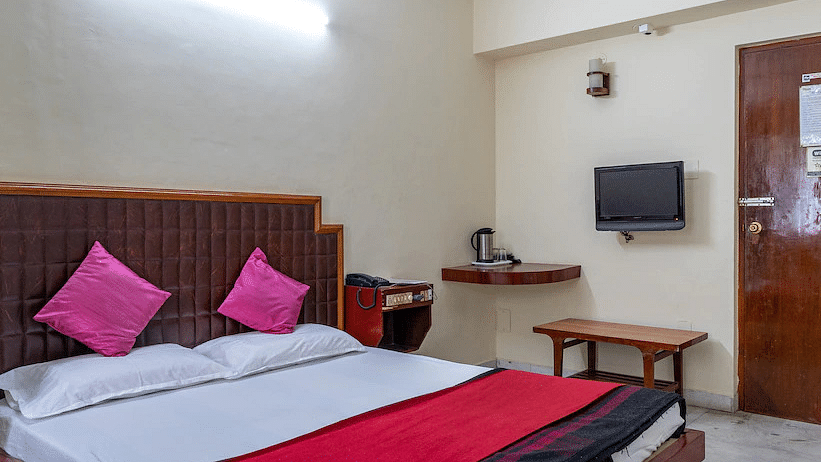 Side angle view of Double room with plush bed, side table and large window - Hotel Ram International,  Pondicherry