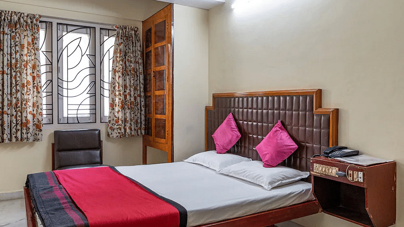 Side view of Double room with plush bed, side table and large window - Hotel Ram International,  Pondicherry