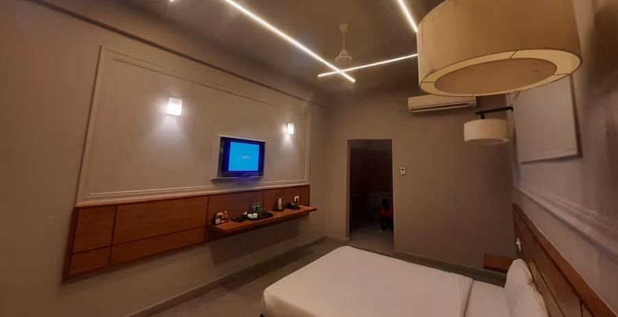 Side view of a room with a bed, TV mounted on the wall, and a lamp - Max Hotel Prayagraj.