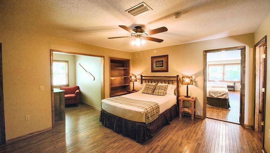 a room with wooden flooring featuring a cozy double bed with a ceiling fan right above it - Historic Tapoco Lodge