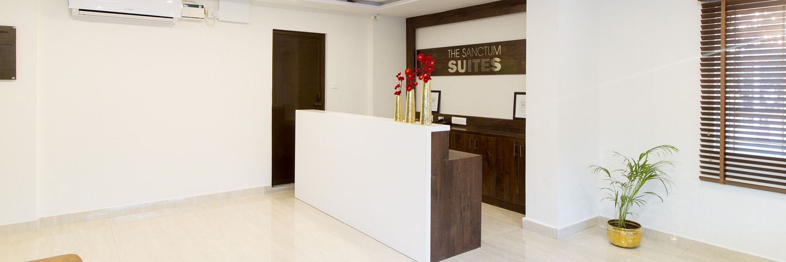 The reception area of Sanctum Suites Whitefield, Bangalore showing a white desk and potted plants for decoration.