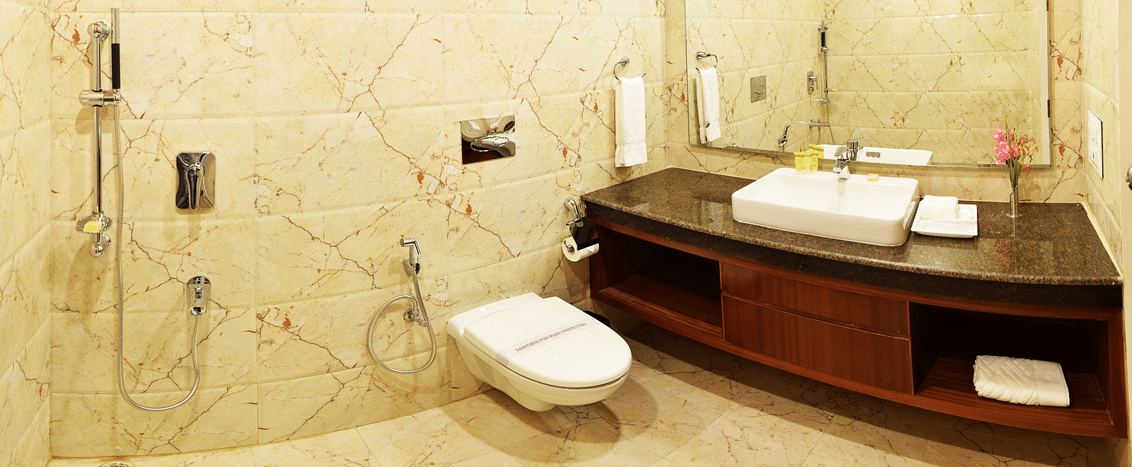 A shot hotel bathroom with a marble-tiled wall, a large mirror, and a sleek vanity  | DLS Serenity Resort and Spa