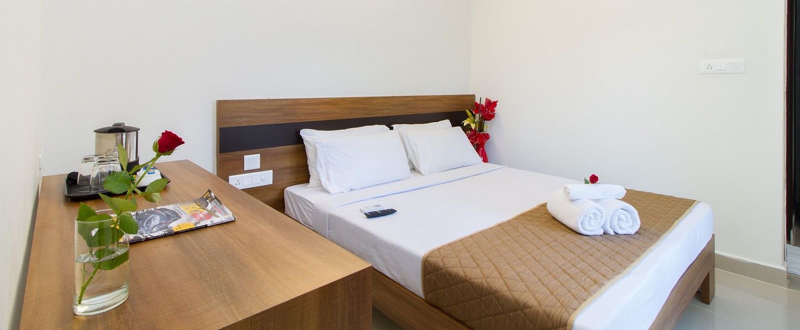 A hotel room at Sanctum Suites Whitefield, Bangalore showing a double bed with white linens and including a table with flowers.