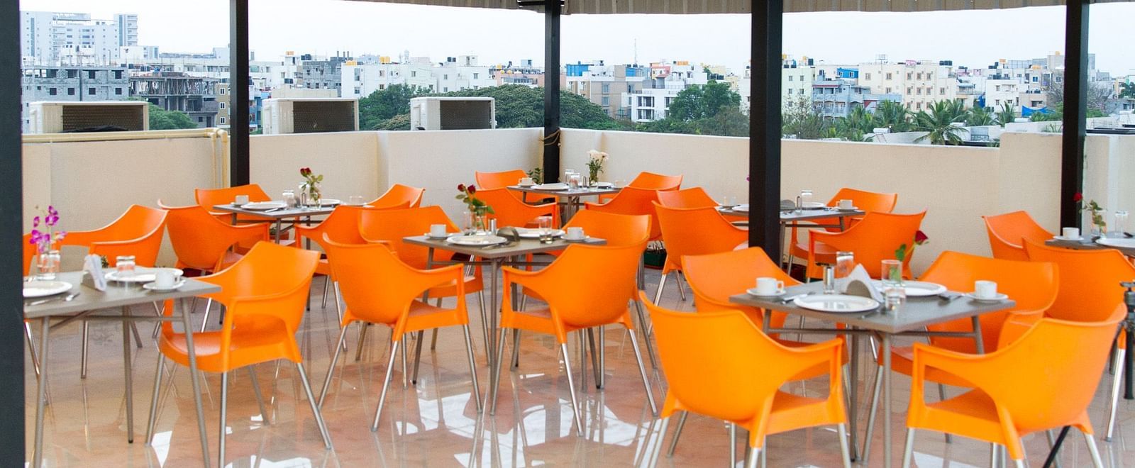 A rooftop dining area featuring numerous tables with bright orange chairs under a metal canopy at Sanctum Suites Whitefield, Bangalore.