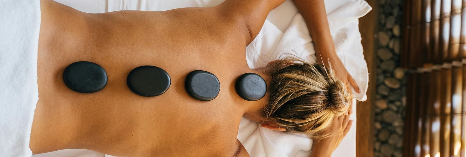 A woman lying down with back with black stones kept over her spine.
