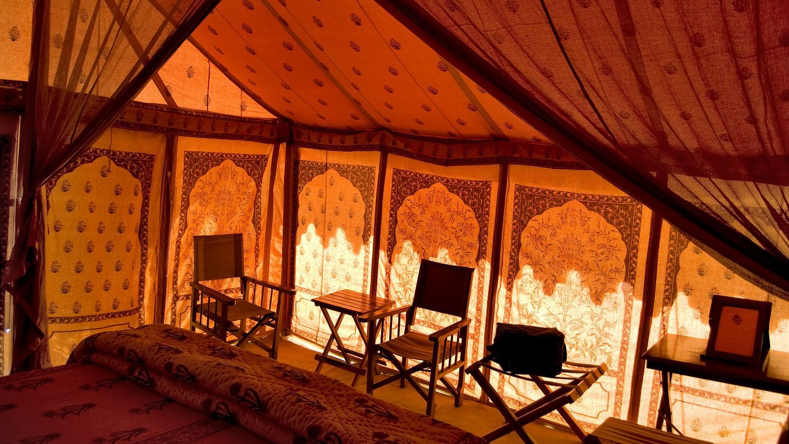  Inside a tent, the romantic glow of the interior lighting reveals intricate patterns on the fabric and a traditional seating area, evoking the ambiance of a bygone era - MANVAR Resort & Desert Camp