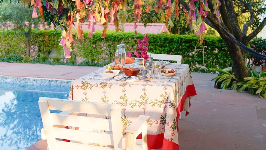 Poolside dining area with a tree decorated with crepe paper on one side, and a table set with a tablecloth and cutlery at Neer Ganga.