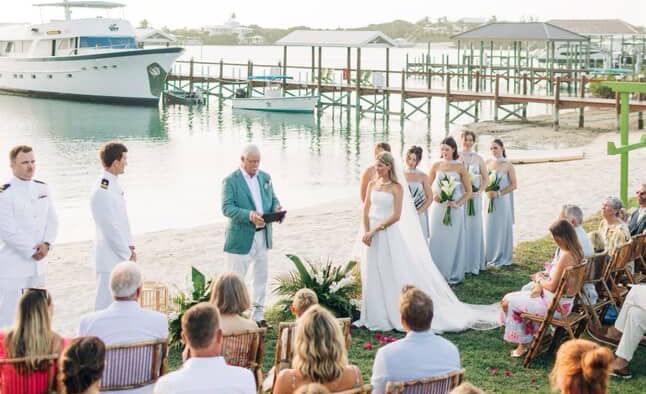 Ceremony attendees sit beside water and watch a wedding event, with a boat and dock in the background at Abaco Inn.