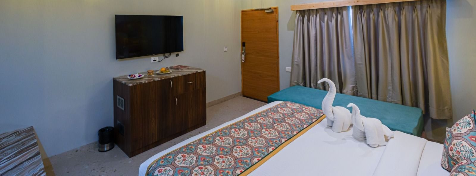 Guest room at Bamboo Saa Resort & Spa, Udaipur with TV, seating area and patterned bed runner.