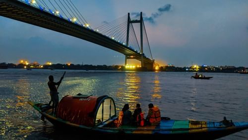 a boat with people on it travelling on a waterbody in front of the howrah bridge in Kolkata.