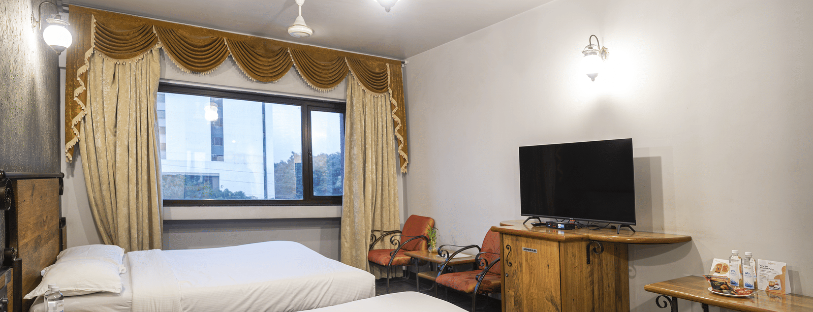 Room with 2 double beds, curtains draped on both the sides of the window, a wooden desk with a television and seating area at Infiniti Hotel, Indore.