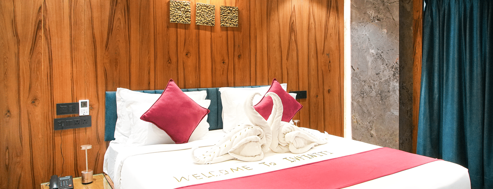 Wooden-panelled bedroom with king bed, red cushions, and dark curtains at Infiniti Hotel, Indore.