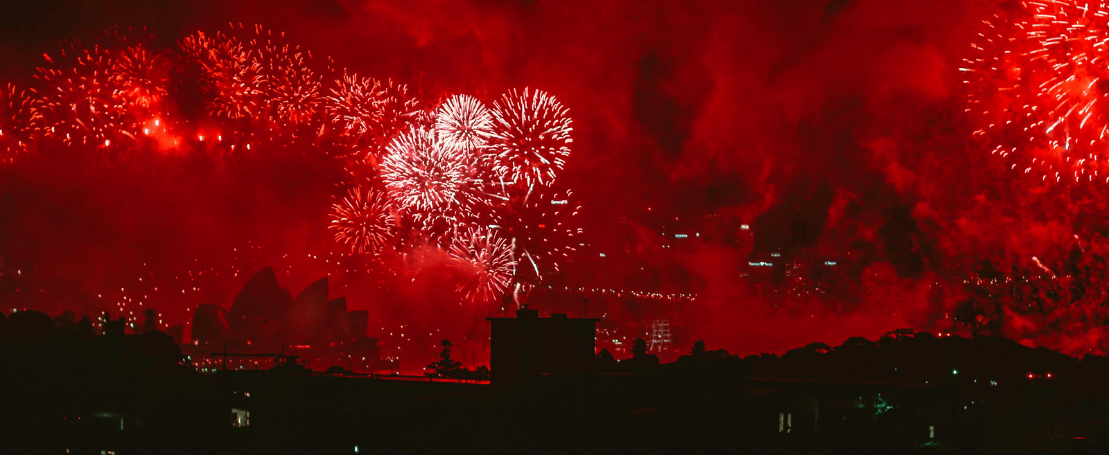 An immense, mostly red fireworks display over a dark city skyline.