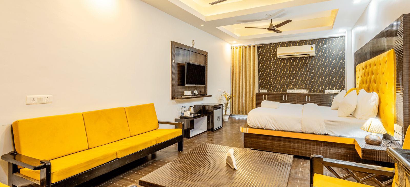 Yellow sofa in the living area and the king size bed with television in front of it at Lime Tree Hotels and Banquet Hall Near Huda Metro, Gurgaon