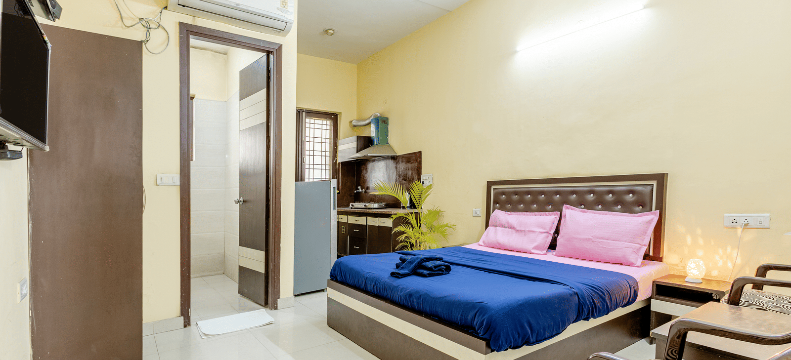 An image of a bedroom featuring a king size bed, a wardrobe, a bedside table, a seating area with chairs and tables,  and a small kitchenette - Lime Tree Studio Serviced Apartment, Gurgaon