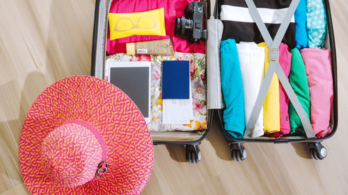 Open suitcase packed with clothes, travel accessories, camera, and beach hat for a holiday.