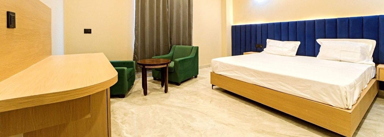 Modern guest room at Grassfield Riveria Resort, Jaipur, featuring a large bed, seating area, ceiling fan, and warm lighting.