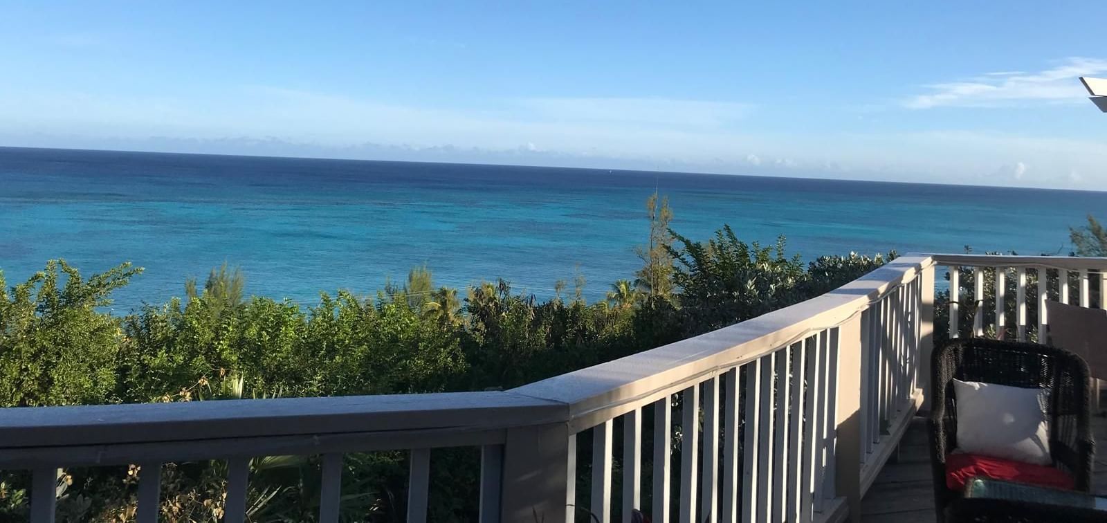 View of the ocean and trees from a deck with a chair and railing | A Stone's Throw Away