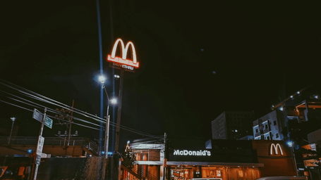 A McDonald's restaurant illuminated at night with its iconic golden arches sign glowing against a dark sky, surrounded by city streets and buildings