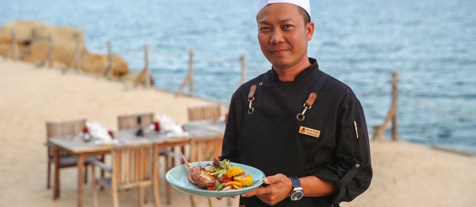 An image of a chef posing with a dish at the riverside An image of a huge sitting area of with several chairs and centre tables - Alibu Resort Nha Thrang