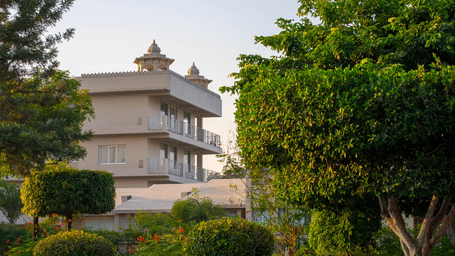 The resort building of Bamboo Saa Sunrrise Wedding & Wellness Resort, Jaipur, surrounded by landscaped gardens and trees against a clear sky.