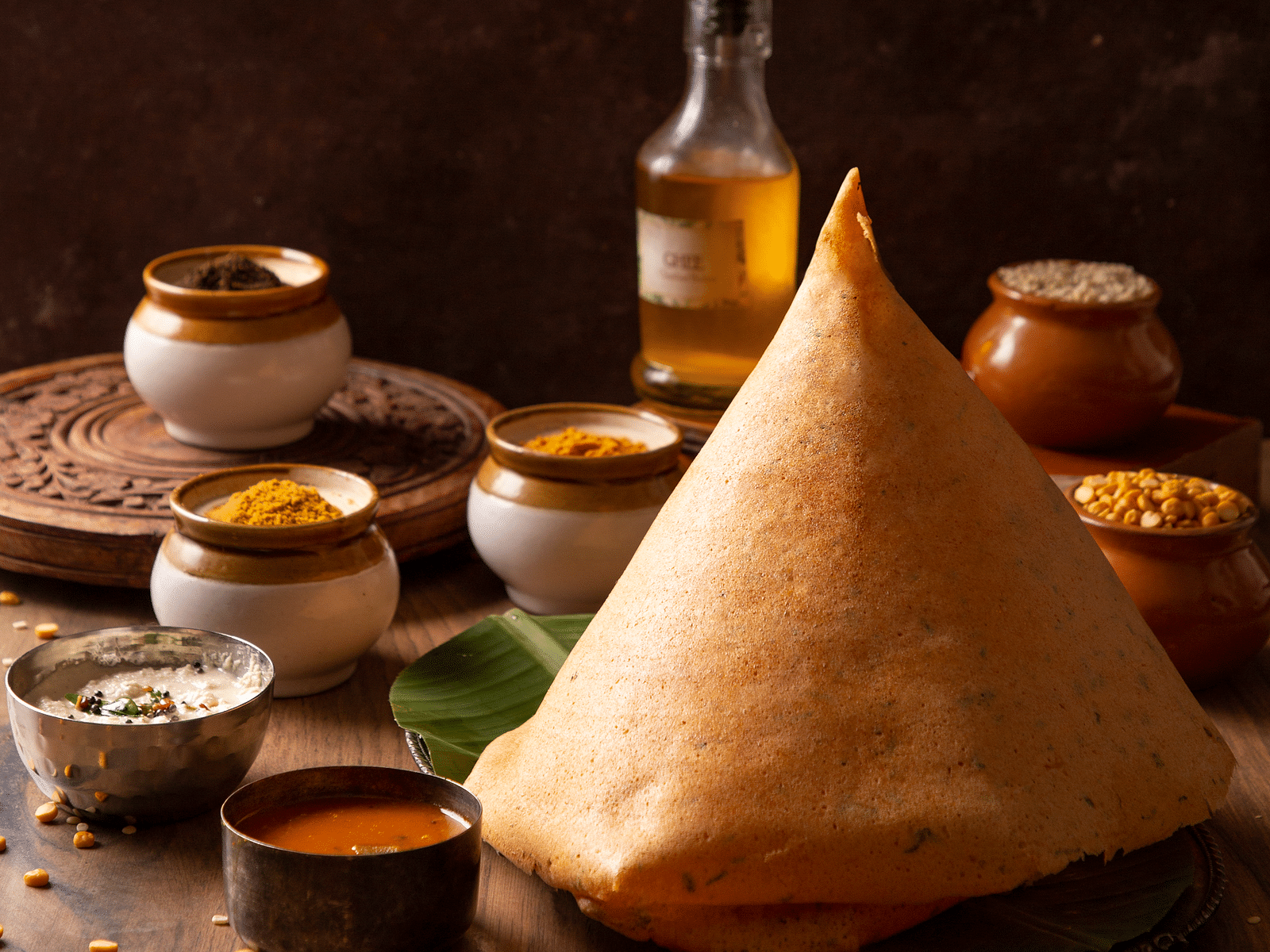 An image of a dosa placed at a table along with sambaar, and various other dishes and curries