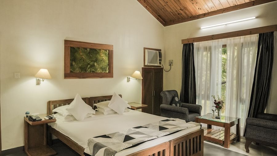 A bedroom with a bed, a lamp, and warm lighting, wooden interior - The Den Corbett Resort & Spa, Kumeria.