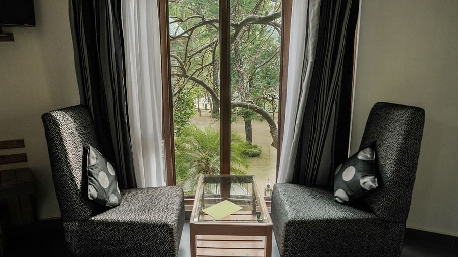 A room with a couch, a chair, and a view of a garden - The Den Corbett Resort & Spa, Kumeria.