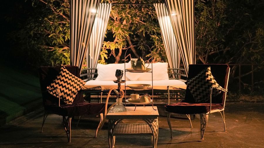 An outdoor seating area with a table and chairs, lit by string lights and fabric canopies - The Den Corbett Resort & Spa, Kumeria.