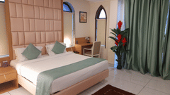 An elegant bedroom with a large bed, work desk & chair, and green curtains - VITS ExcellenSea, Dapoli