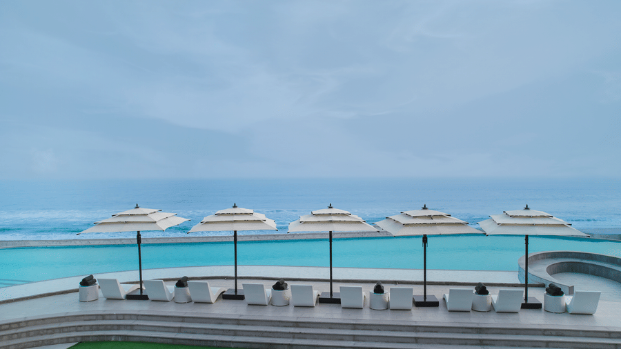 An outdoor pool area at Swosti Premium Beach Resorts, Puri, with several white umbrellas, lounge chairs, and a pool overlooking the sea.