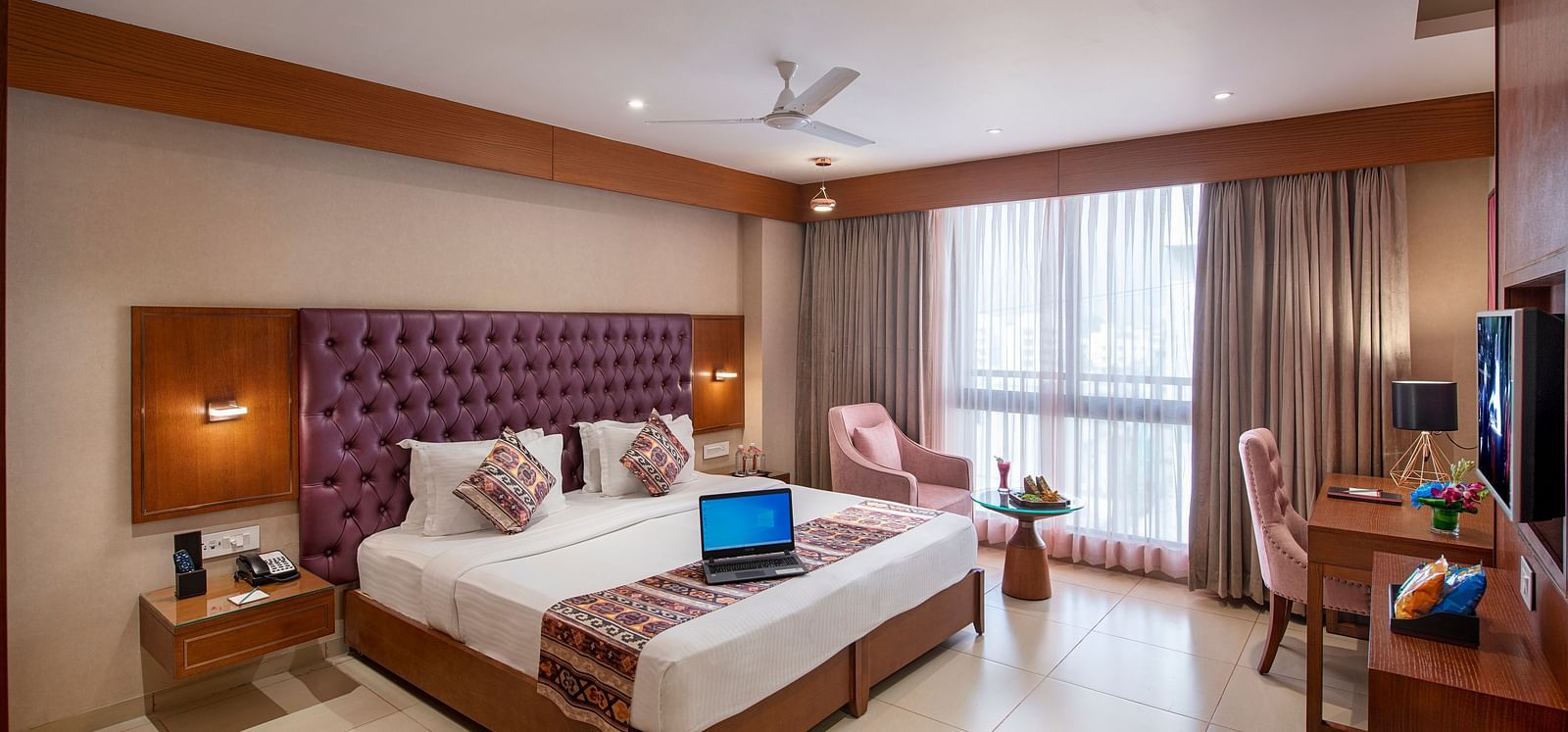 A spacious hotel room with a large bed, seating area, and city views - SK Lords Inn Ahmedabad