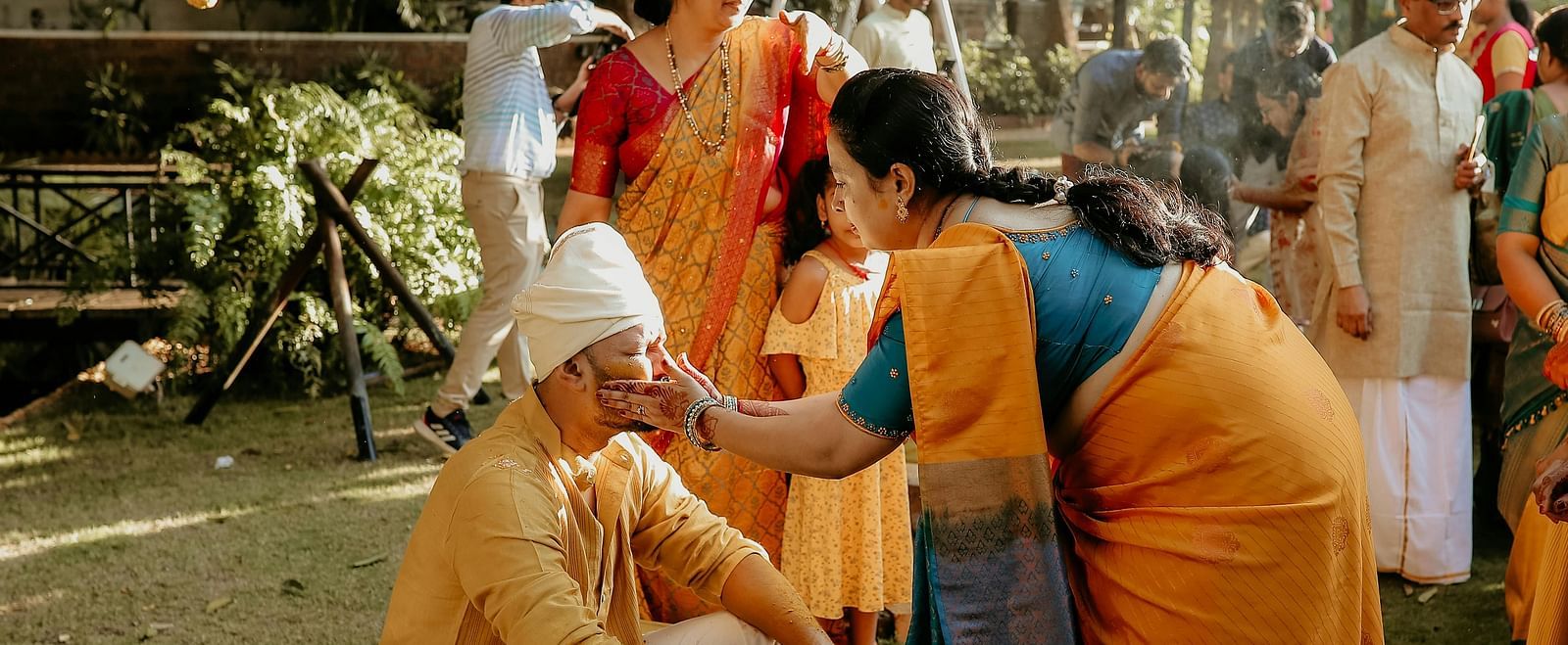 The Indian wedding ritual of haldi being performed in a lawn where a woman is applying turmeric on the groom.