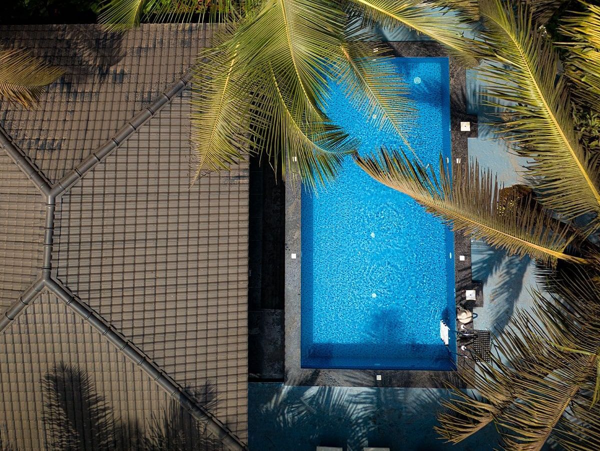 A view from above, looking down at a bright blue swimming pool surrounded by greenery and the side of Kssemya.