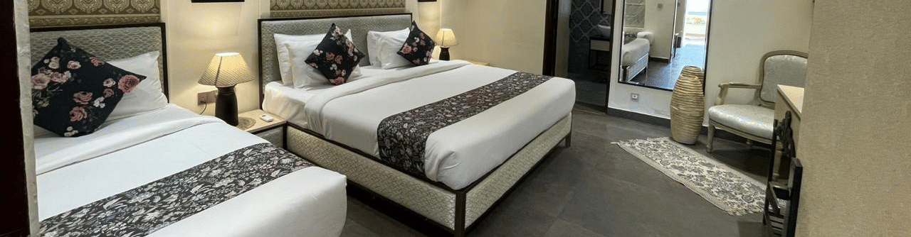 2 single beds with wall decor and lamps beside a mirror and armchair at Beelwa Palace, Jaipur