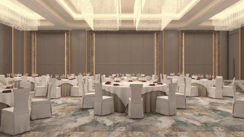 Banquet hall at Tulip Inn Bidar with 8 round dining tables, chairs with fabric covers, lit ceiling fixtures, and patterned carpet flooring.