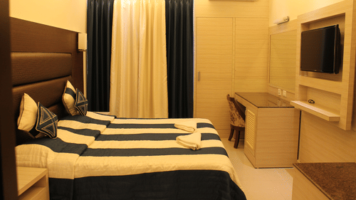 Interiors of the Deluxe Room at Hotel Shompen featuring a double bed, wall-mounted TV, and elegant blue and white curtains, ideal for travellers exploring the best Port Blair hotel deals.