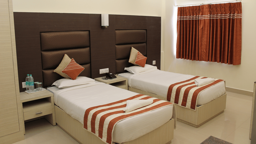 Interiors of a Deluxe Room at Hotel Shompen, offering the finest stay in Port Blair, featuring twin beds with upholstered headboards and a window with its curtain closed.